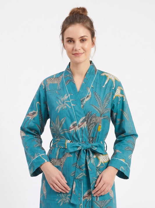 A woman modeling a teal blue tropical print bathrobe with a matching tie belt, set against a plain white studio background.
