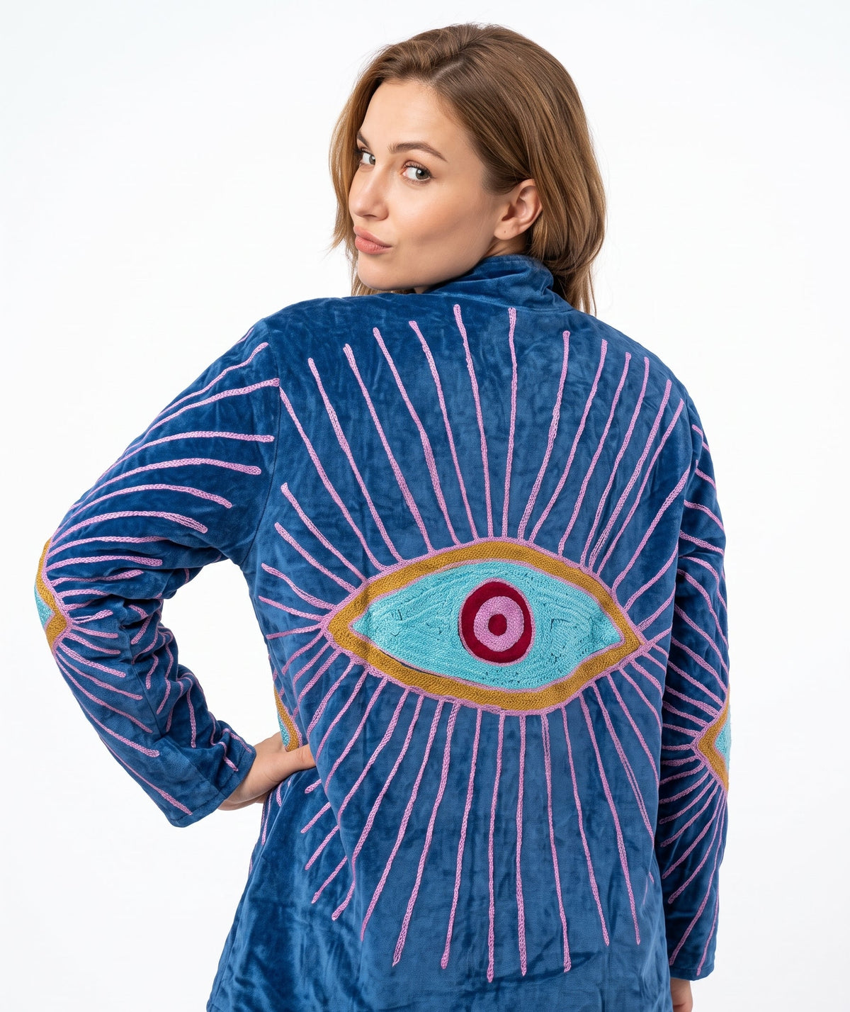 A woman wearing a blue plush zip-up jacket with a large embroidered eye design on the back, shown against a plain white studio background.