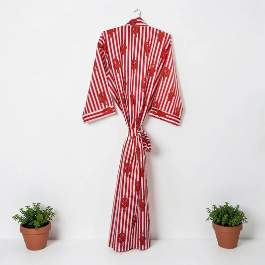 Red and white striped robe with a pattern on a hanger against a white background, flanked by two potted plants.